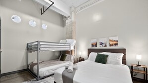 A modern hotel room with a bunk bed, a large bed, and a nightstand with a lamp. - Modern Downtown 2BR | Pool, Laundry, Valet Parking (Dallas)