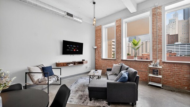 A modern living room with a flat-screen TV, a sofa, a coffee table, and a dining area with a table and chairs. - Modern Downtown 2BR | Pool, Laundry, Valet Parking (Dallas)