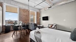 A modern hotel room with a large bed, a sofa, a dining table, and a TV. - Walk to Convention Center | Pool + Valet Parking (Dallas)