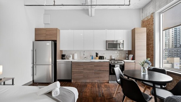 A modern kitchen with stainless steel appliances, a wooden island, and a dining area with a round table and chairs. - Walk to Convention Center | Pool + Valet Parking (Dallas)