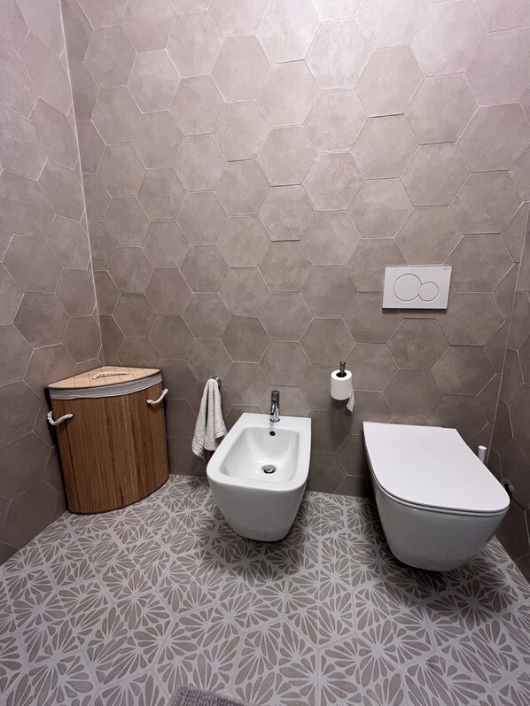 A bathroom with a hexagonal tile wall, a wooden bidet, a white sink, and a toilet. - Bay of Saracens, renovated apartment 6 people with garden parking space (Varigotti)