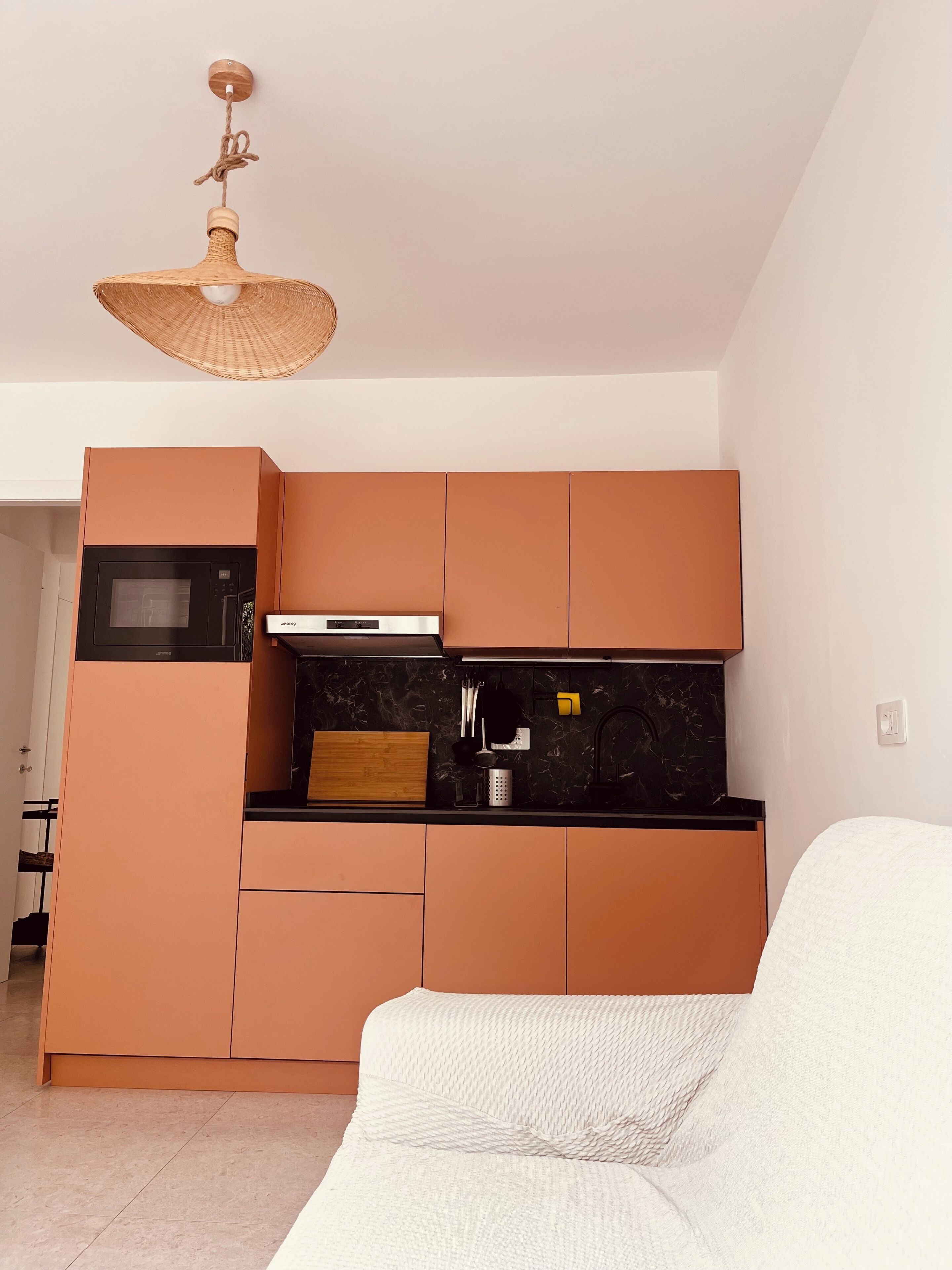 A modern kitchen with built-in appliances, a hanging light fixture, and a white sofa in the living area.