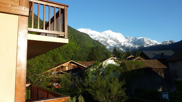 Een houten balkon met uitzicht op een berglandschap met besneeuwde toppen.
