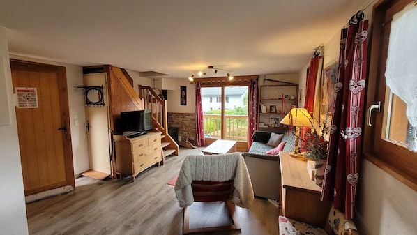 Una sala de estar acogedora con chimenea, televisor, comedor y balcón con cortinas rojas.