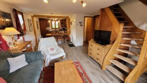 Una sala de estar acogedora con un sofá, una silla, un aparador de madera, un televisor y una escalera.