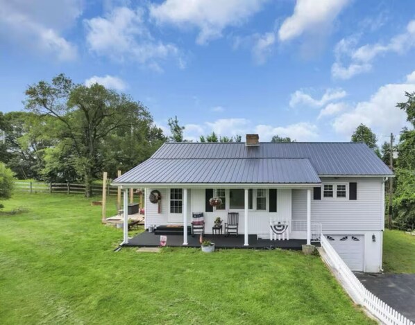 A single-story house with a metal roof, a porch with a railing, and a garage. - Ridgeview Cottage - 6 miles to the Rock House! (Laurelville)
