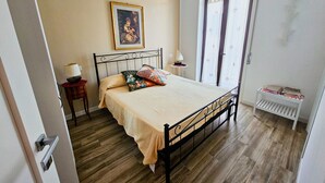 Un dormitorio con cama, mesita de noche, lámpara, ventana con cortinas y radiador.