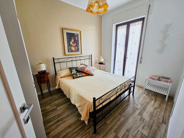 Een slaapkamer met een bed, een nachtkastje, een lamp, een raam met gordijnen en een radiator.
