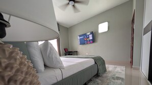Ett hotellrum med en säng, en tv som är monterad på väggen, en fjärrkontroll på ett bord och en lampa.