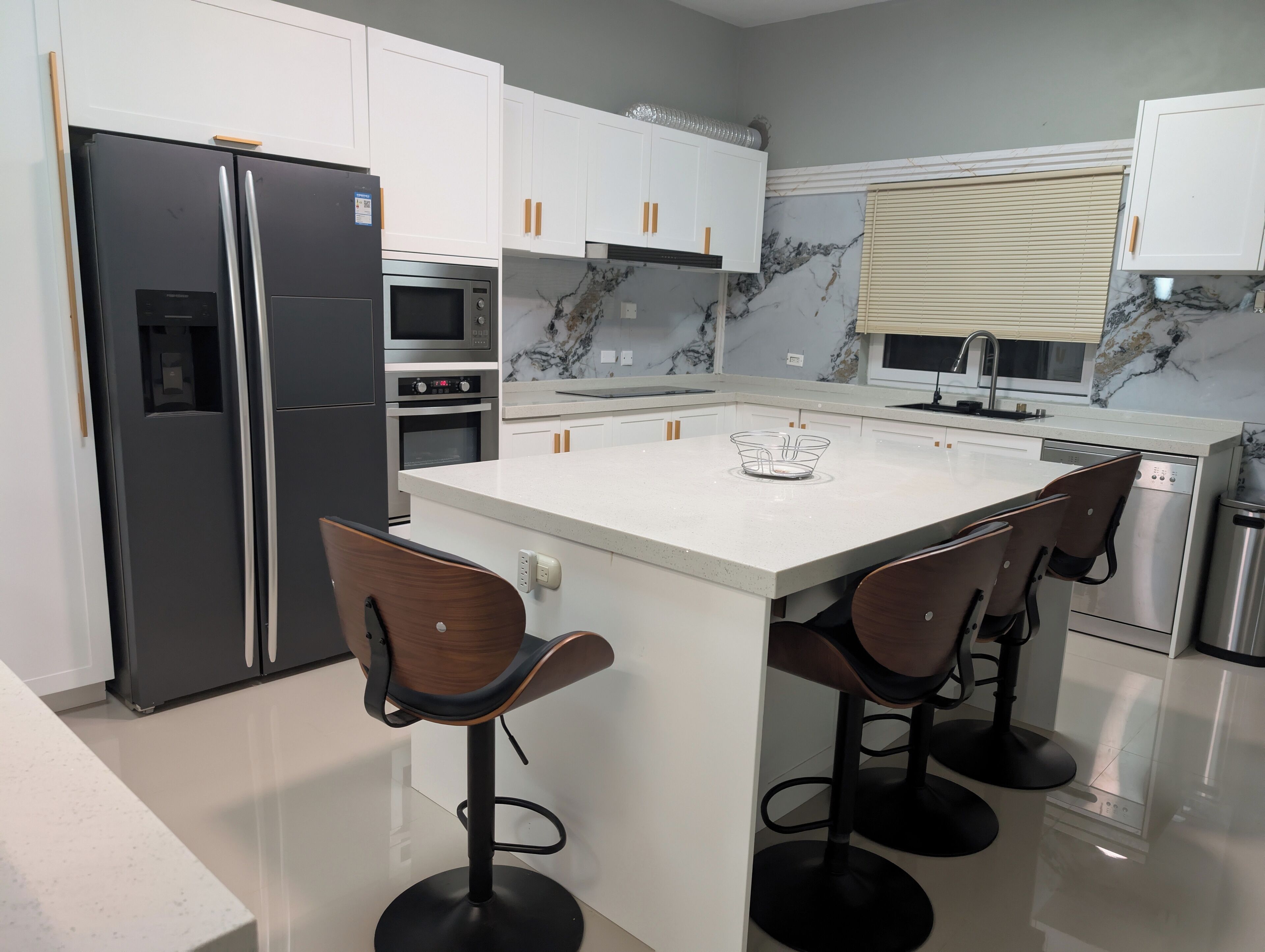 A modern kitchen with white cabinets, a black refrigerator, a built-in oven, a microwave, and a stainless steel dishwasher. There is a central island with bar stools.