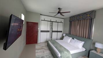 Ein Schlafzimmer mit Bett, Deckenventilator, Kleiderschrank, Fernseher und einer Tür.