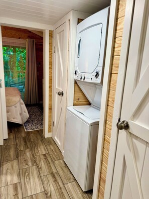 Une pièce de taille modeste équipée d’un lave-linge, d’un lit recouvert d’une courtepointe à motifs et dotée d’un plancher en bois.
