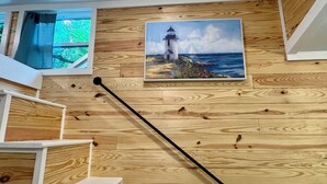 A wooden staircase with a painting of a lighthouse and ocean view on the wall. - New cottage with Hot Tub, Tiki Bar, Sauna, and Plunge Tub. Million Dollar Views (Brevard)