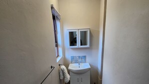 Un pasillo estrecho con un lavamanos blanco, un espejo y una toalla colgada en la pared.