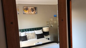 Un dormitorio con cama, mesita de noche, lámpara y espejo.