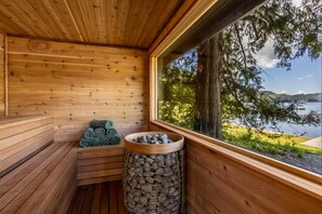 A wooden sauna with benches, a stack of towels, and a stone-filled container.