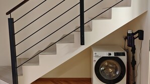 A modern interior with a wooden herringbone floor, a white washing machine, and a black metal staircase.