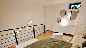 A bedroom with a bed, a bedside table, a mirror, and a small window.