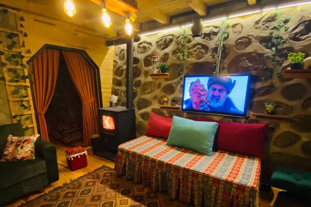 A cozy room with a stone wall, a fireplace, a television, and a patterned rug.