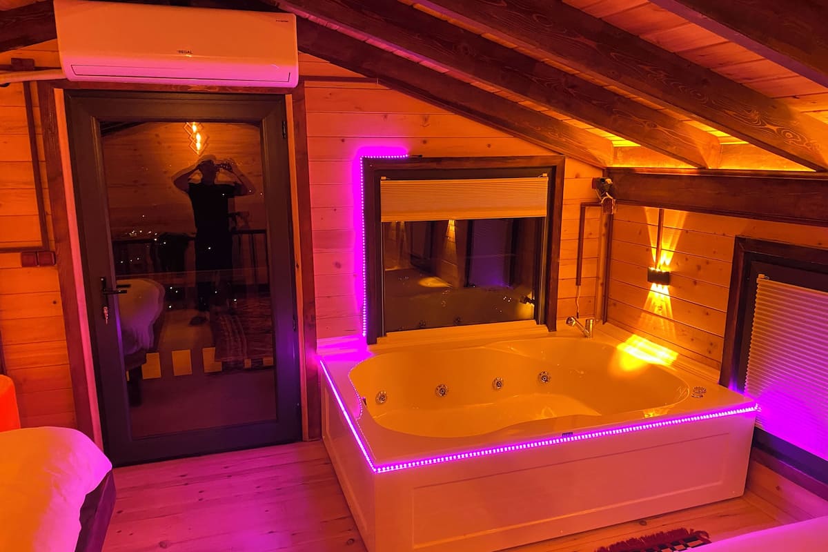 A room with a large bathtub, wooden walls, and a ceiling fan.