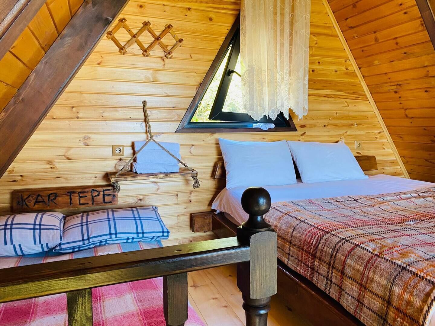 Un dormitorio de cabaña acogedor con cama, almohadas, un perchero y una ventana con cortinas.