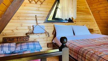Un dormitorio de cabaña acogedor con cama, almohadas, un perchero y una ventana con cortinas.