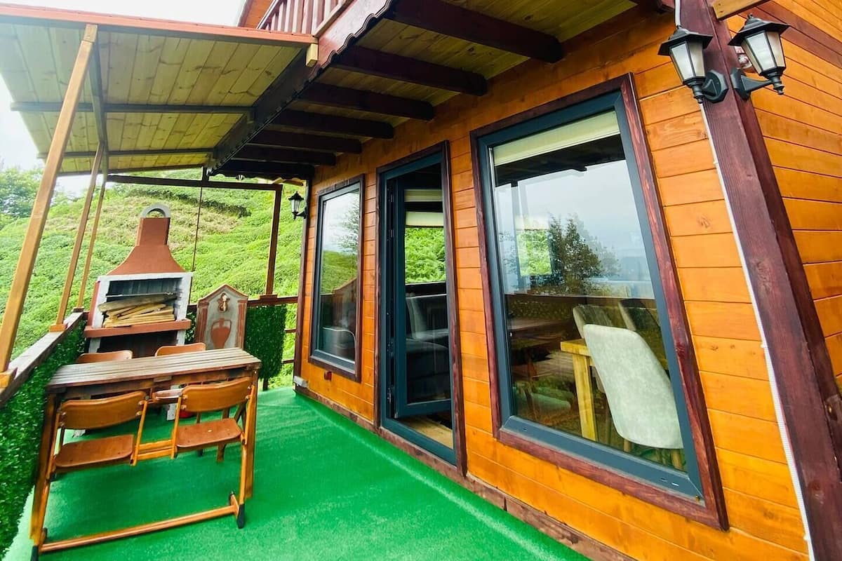 A wooden cabin with a covered patio, a grill, and large windows.