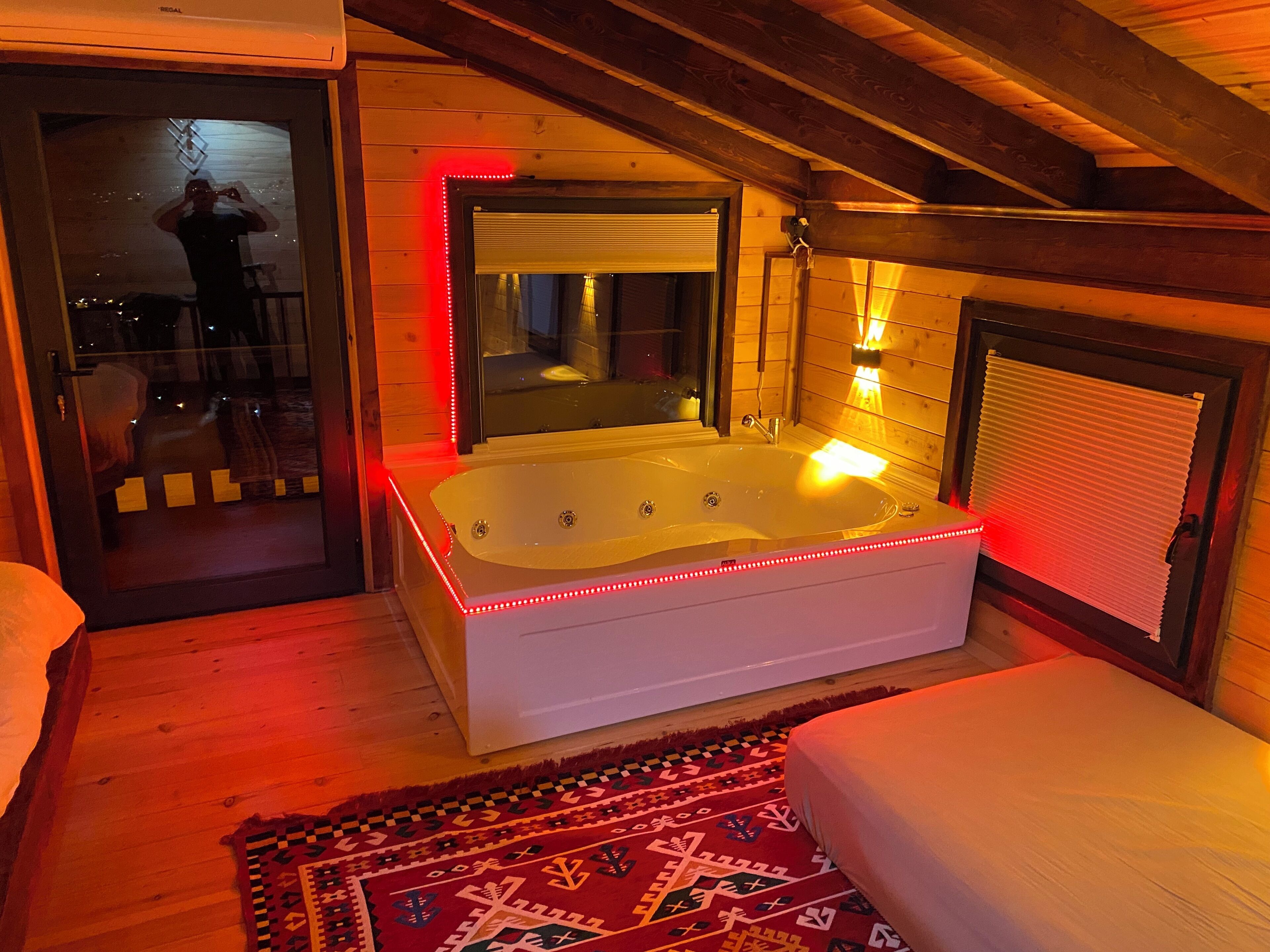 A room with a large bathtub, a mirror, and a window with blinds.
