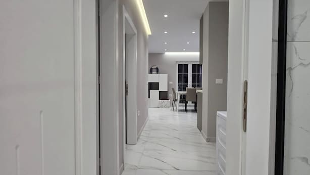 A modern hallway with white walls and marble flooring, leading to a room with a large window and a dining area. - Prestige Beach Apartament Durres (Durres)