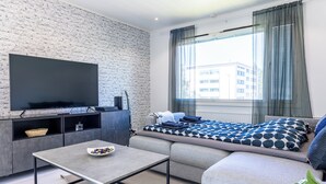 A modern living room with a sofa, a flat-screen TV, a coffee table, and a window with curtains.
