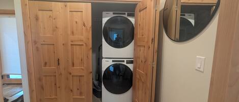 Ett tvättrum med två Whirlpool-tvättmaskiner placerade ovanpå varandra och en dörr av trä.