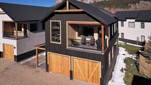 Une maison moderne à deux étages, dotée d’un balcon, de grandes fenêtres et d’un garage.