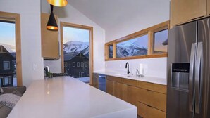 Une cuisine moderne dotée d’un îlot central, de meubles en bois, d’appareils électroménagers en acier inoxydable et de grandes fenêtres offrant une vue sur les montagnes.