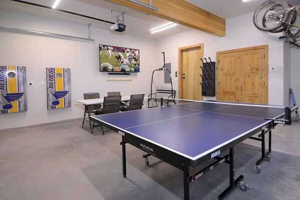 A ping pong table in a room with a projector, chairs, and artwork on the walls.