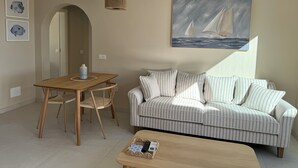 A living room with a striped sofa, a wooden coffee table, a dining table with chairs, and a painting of sailboats on the wall. - Tortuguero vacation apartment: air conditioning and sea views, ideal for couples (Morro Jable)