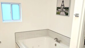 A modern bathroom with a large bathtub, a window, and a picture of the Eiffel Tower.