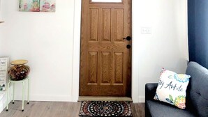 A room with a wooden door, a small table with a glass top, a cushion with a floral pillow, and a welcome sign on the wall.
