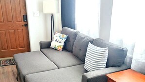 A cozy room with a grey sofa, a wooden side table, and a wooden door.
