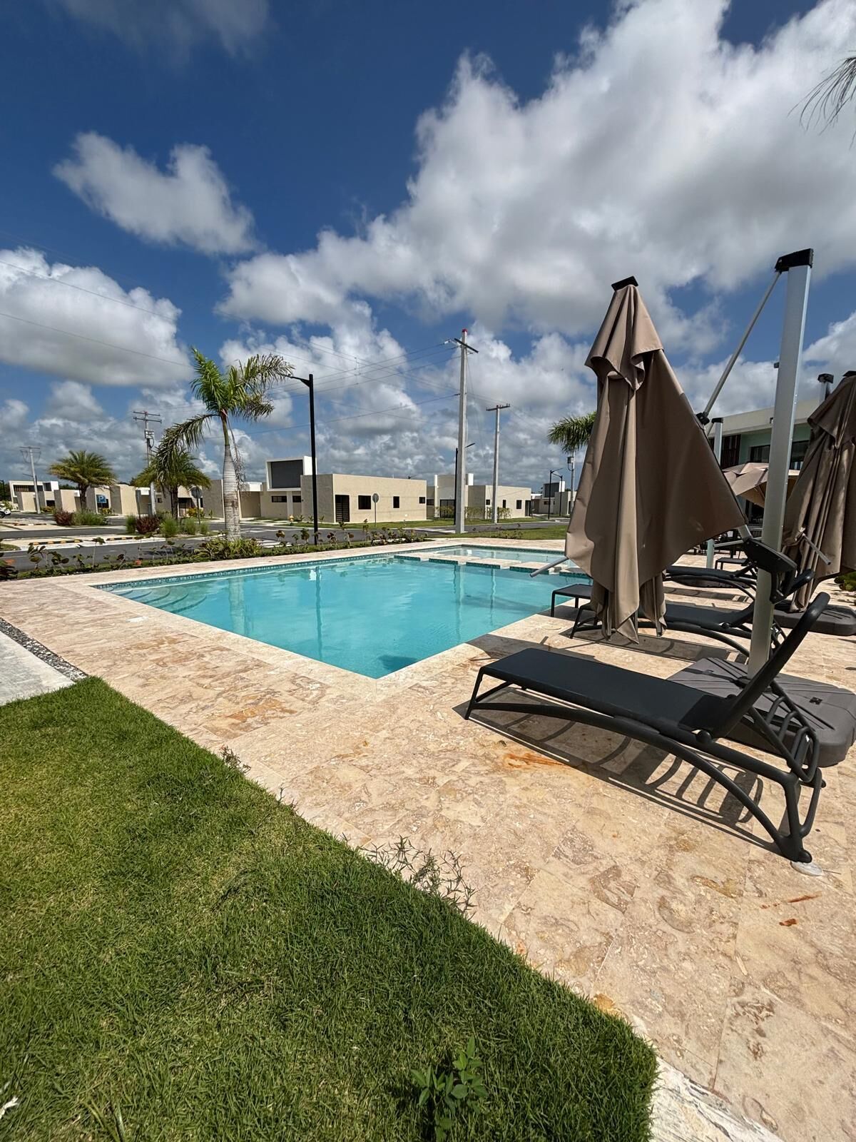 Ein Pool mit Liegestühlen und Sonnenschirmen, umgeben von einer gepflegten Rasenfläche und Gebäuden im Hintergrund.
