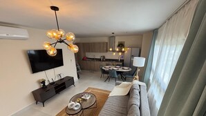 A modern living room with a sofa, coffee table, and TV. There's a dining area with a table and chairs, and a kitchen in the background. - The Windown Suite Near Downtown Punta Cana (Higuey)