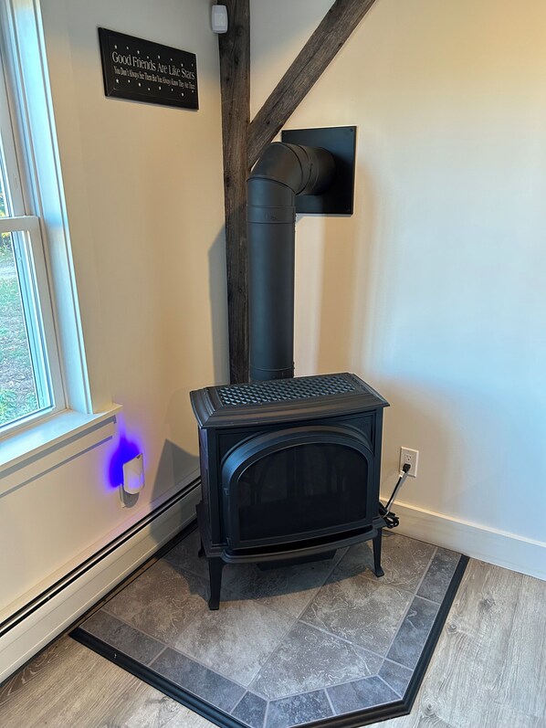 A wood-burning stove in a room with a window, a black sign on the wall, and a tiled floor. - Panoramic Mountain Views (Ossipee)