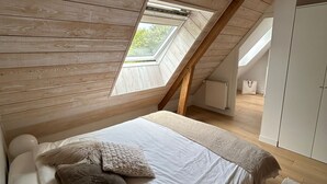 A bedroom with a sloped ceiling, wooden beams, a skylight, a bed with white linens, and a white wardrobe. - 10 mn from Wimereux beach, charming renovated farmhouse in a green setting (Wierre-Effroy)