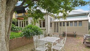 A patio with a table and chairs, surrounded by a brick wall and greenery. - Idlehour - central, cosy classic mountain cottage (Katoomba)