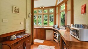 A compact kitchen with wooden cabinets, a built-in dishwasher, a microwave, and a window overlooking greenery. - Idlehour - central, cosy classic mountain cottage (Katoomba)