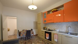 A compact kitchen with orange cabinets, a dining area with a floral tablecloth, and a patterned rug. - B&b on the course, Reggio Calabria (Reggio Calabria)