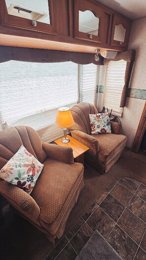 Indretning i en autocamper med to komfortable siddepladser, et lille bord med lampe og et vindue med persienner.