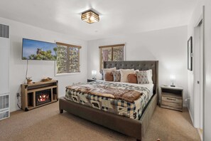 Un dormitorio con cama, chimenea, televisor y ventana con vistas.