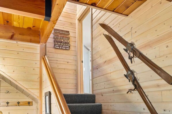 A wooden interior with a staircase, a sign with motivational phrases, and a ski rack.
