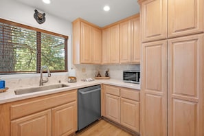 A kitchen with wooden cabinets, a dishwasher, a window with blinds, and a bear head decoration on the wall.