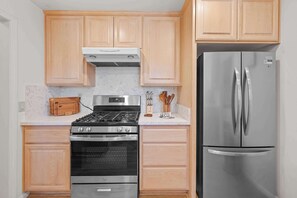 Una cocina con armarios de madera, estufa, horno y refrigerador de acero inoxidable.